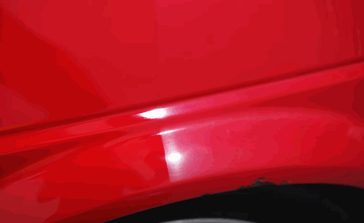 A hand moves across the red car surface to demonstrate the high gloss and mirror-like finish achieved after polishing, showing a dramatic improvement in shine.