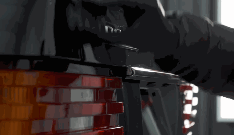 A technician works on a black car using a tool to apply ceramic coating