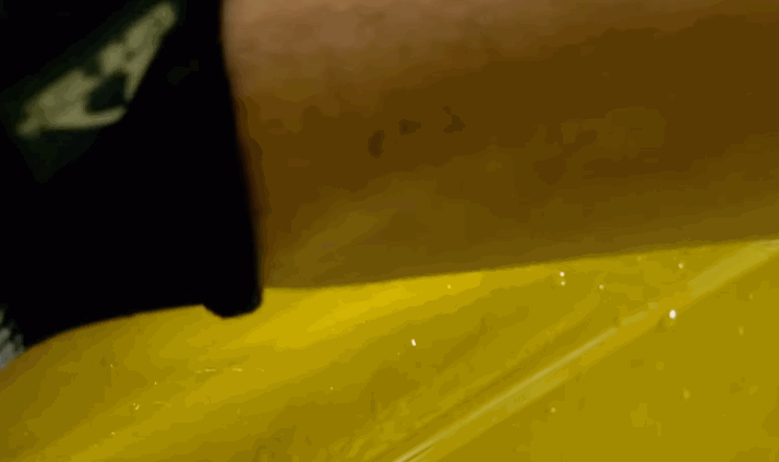 Close-up of a squeegee tool being run across yellow-tinted paint protection film during application to a car panel.